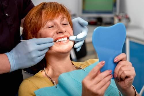 Woman with red hair looking at teeth in mirror, ashburn va
