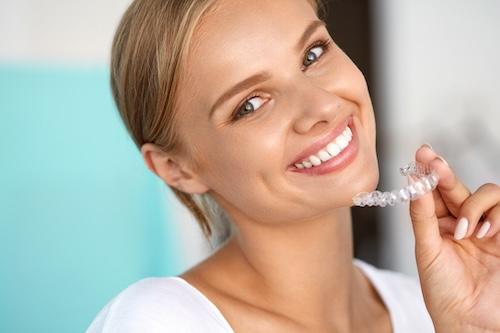 blonde woman smiling holding clear plastic aligner | dentist ashburn va