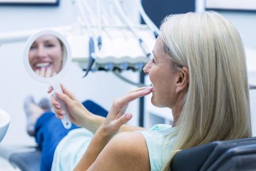 Woman looking at teeth in mirror after cosmetic dentistry, ashburn va